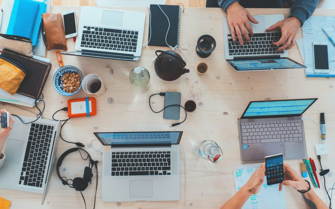 Overhead view of a workspace featuring several laptops, notebooks, and personal items on a wooden table. – SLIMDESIGN